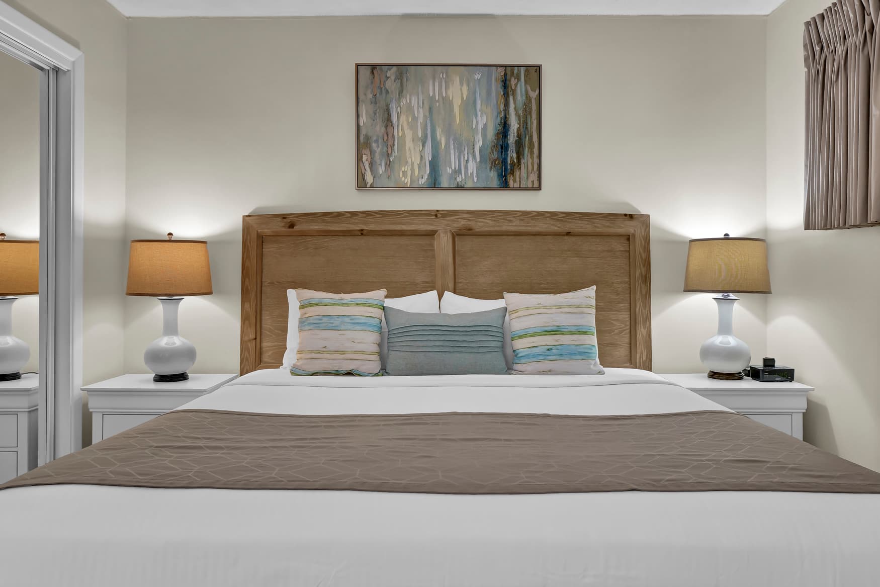 Sink into crisp white linens and plush pillows in your serene bedroom sanctuary, where warm lighting and coastal artwork create the perfect retreat.