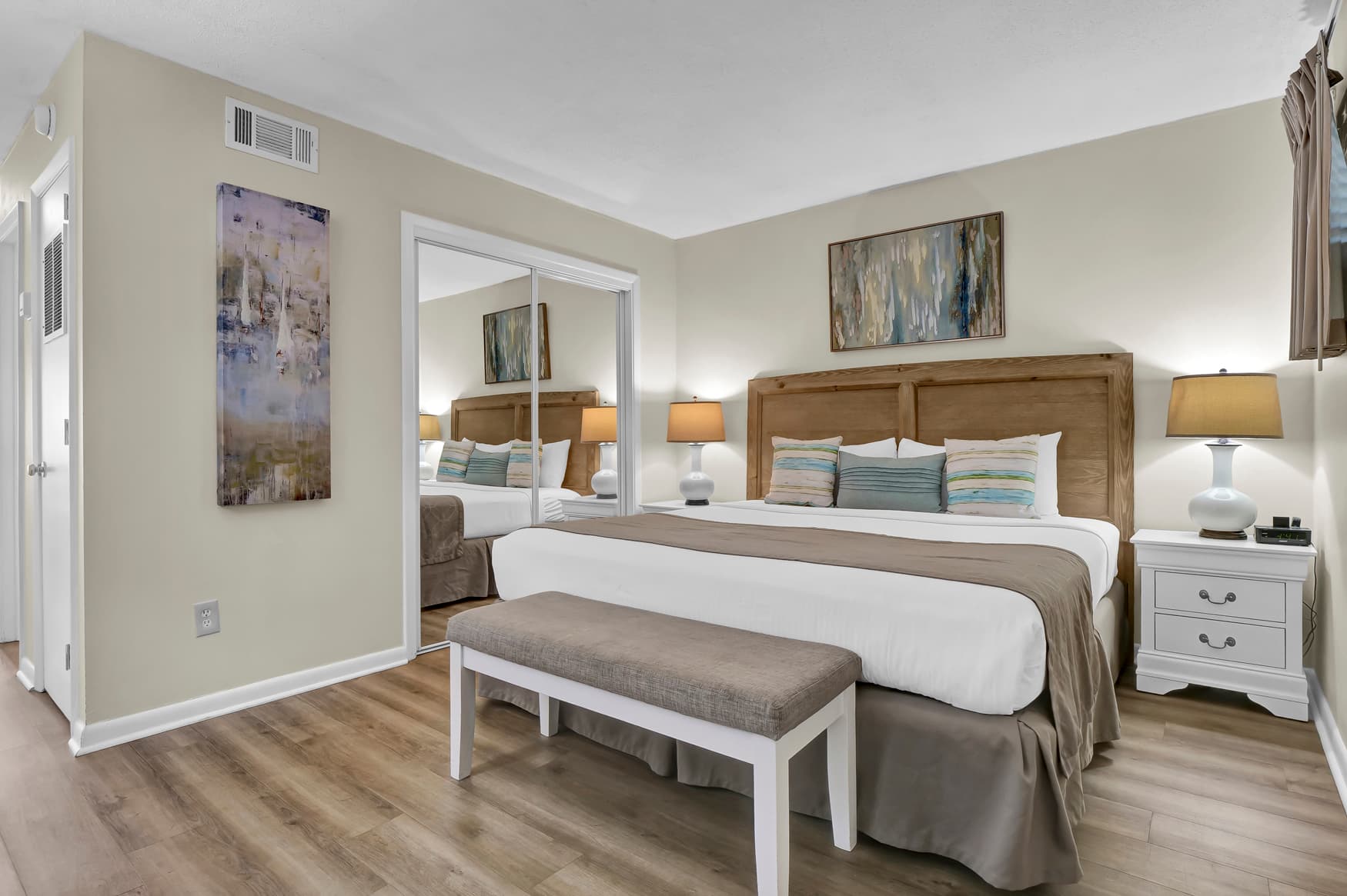 Sink into your luxurious king bed surrounded by coastal artwork and warm lighting that creates the perfect retreat atmosphere.