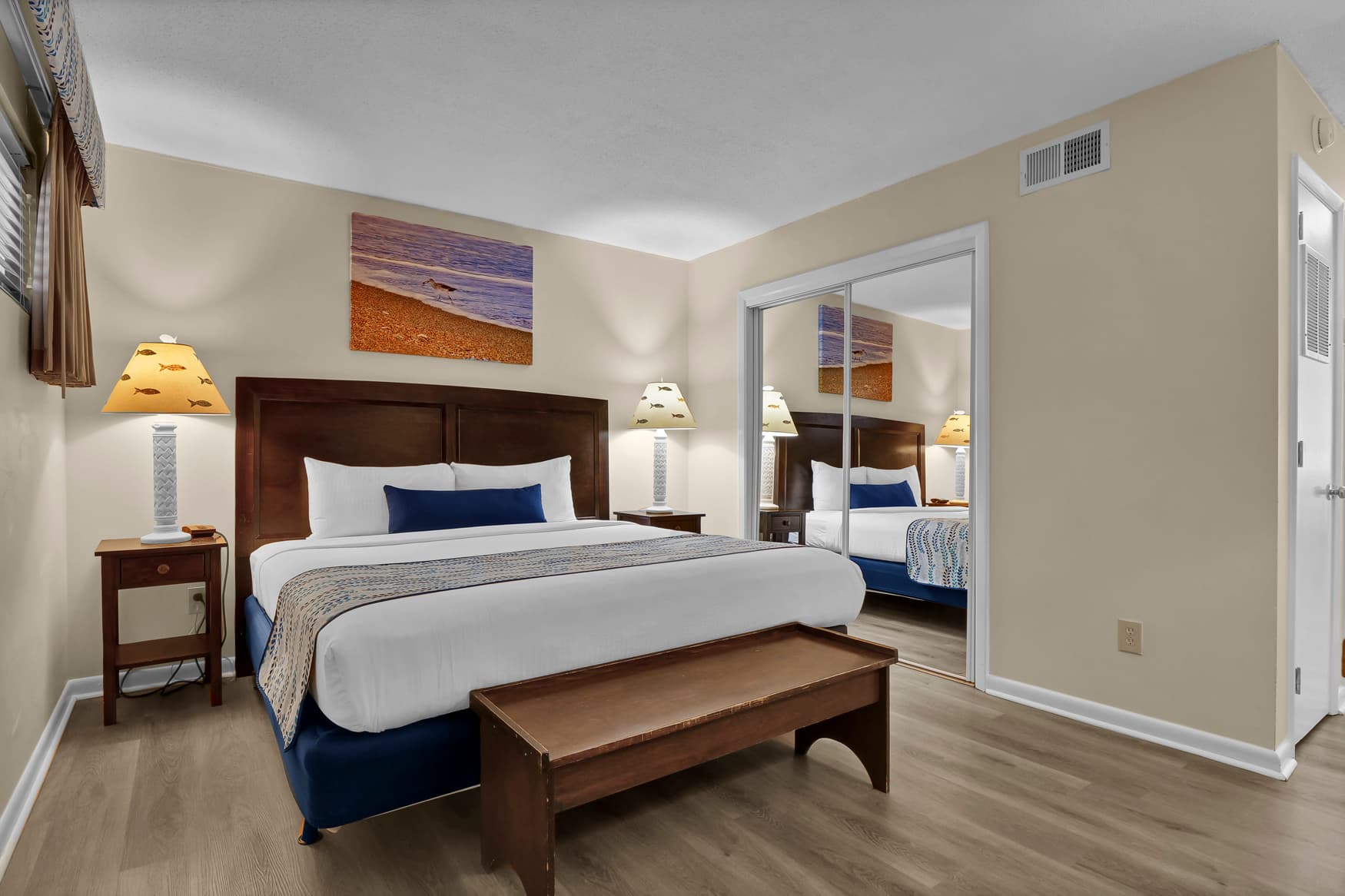 Sink into the comfort of your spacious bedroom featuring a king-size bed with premium linens, warm wood furnishings, and coastal artwork for a relaxing retreat.