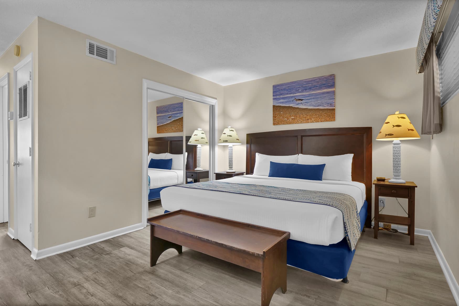 Sink into crisp white linens and plush pillows in your serene bedroom, where coastal artwork and warm lighting create the perfect retreat.