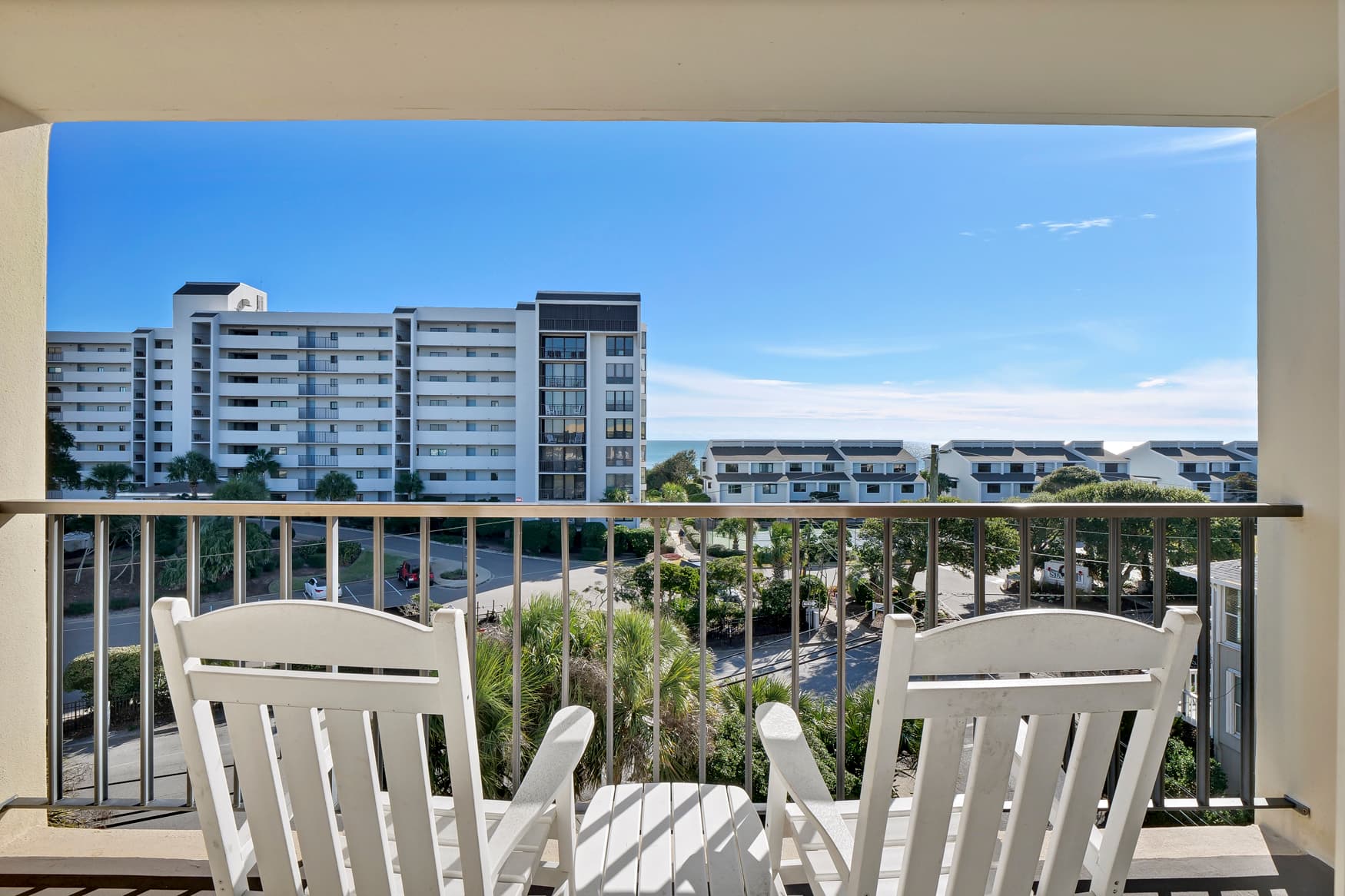 Relax on your private balcony with comfortable seating while enjoying views of the modern neighborhood buildings and lush greenery below.