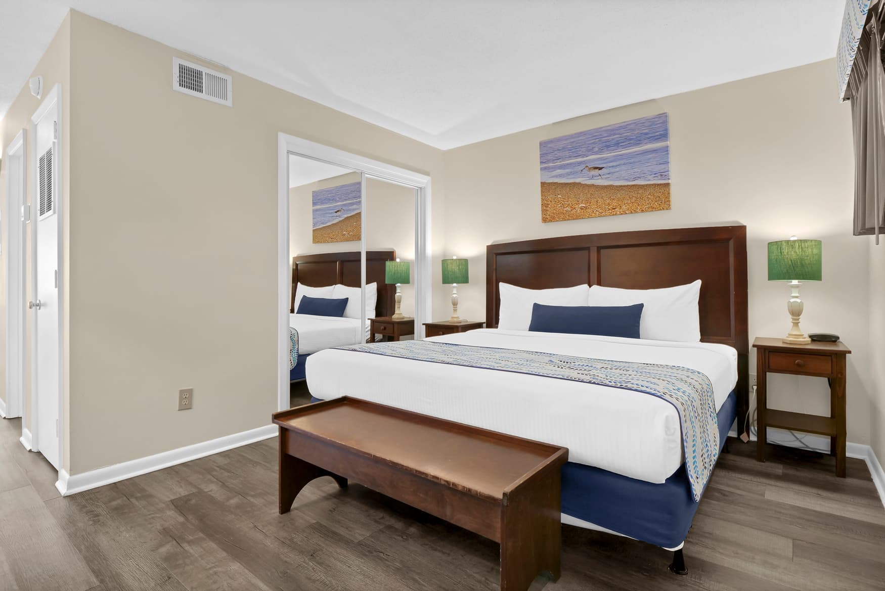 Your spacious bedroom features crisp white linens, coastal artwork, and twin nightstand lamps creating a serene retreat.