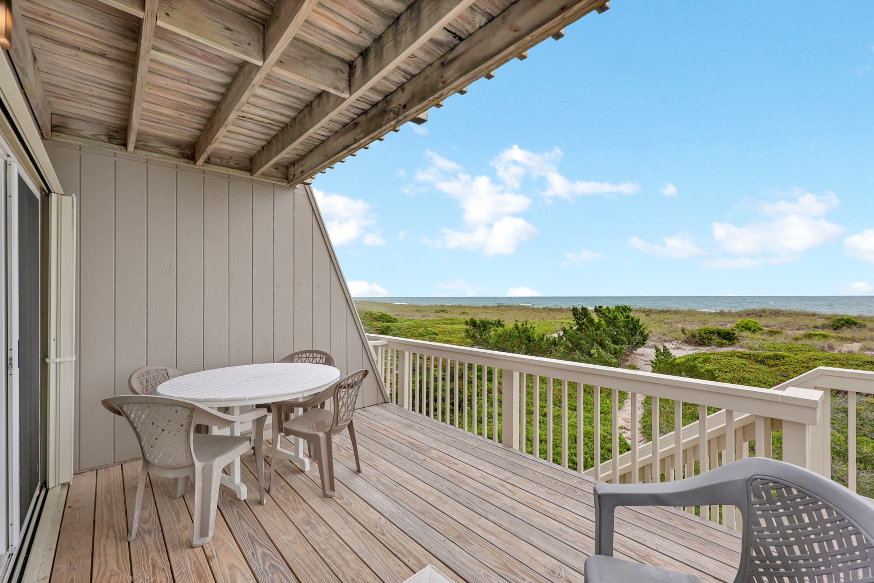 Private deck overlooking coastal dunes and the sea, featuring comfortable outdoor seating and an expansive horizon view under open skies.
