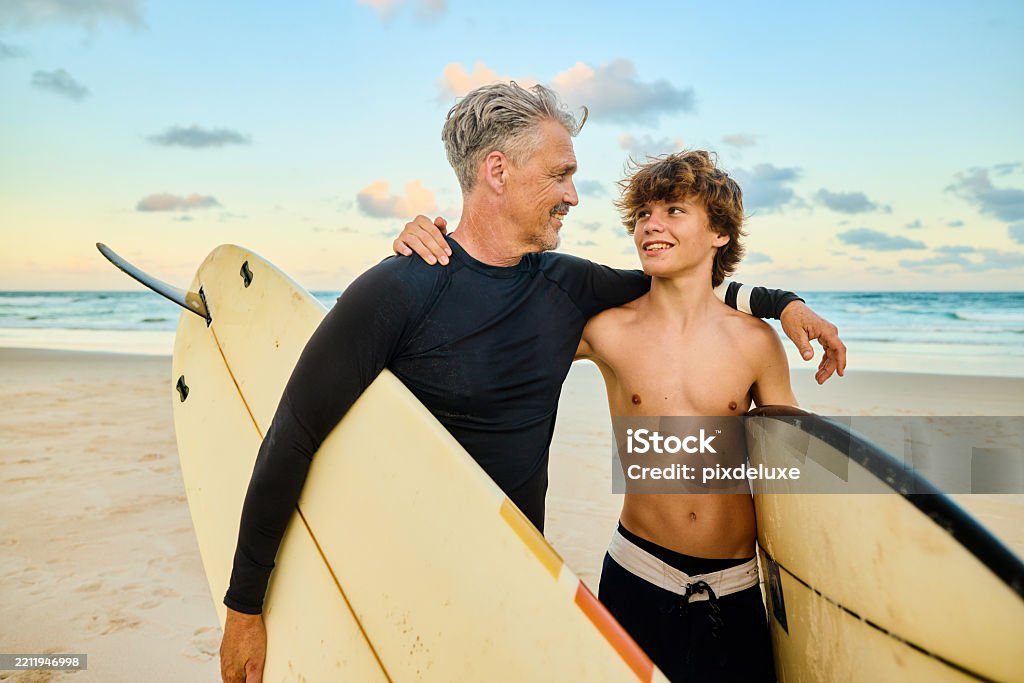 Father and son holding surfboards on the beach at sunset