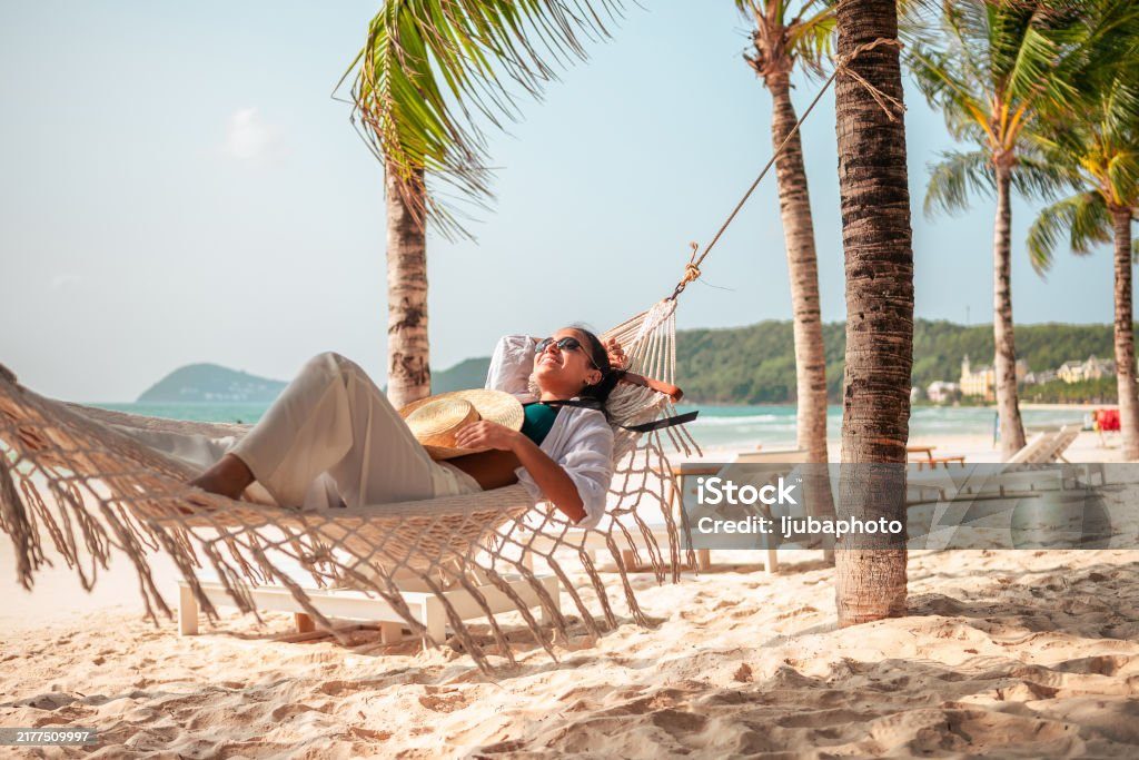 Woman relaxing in a hammock between palm trees by the sea