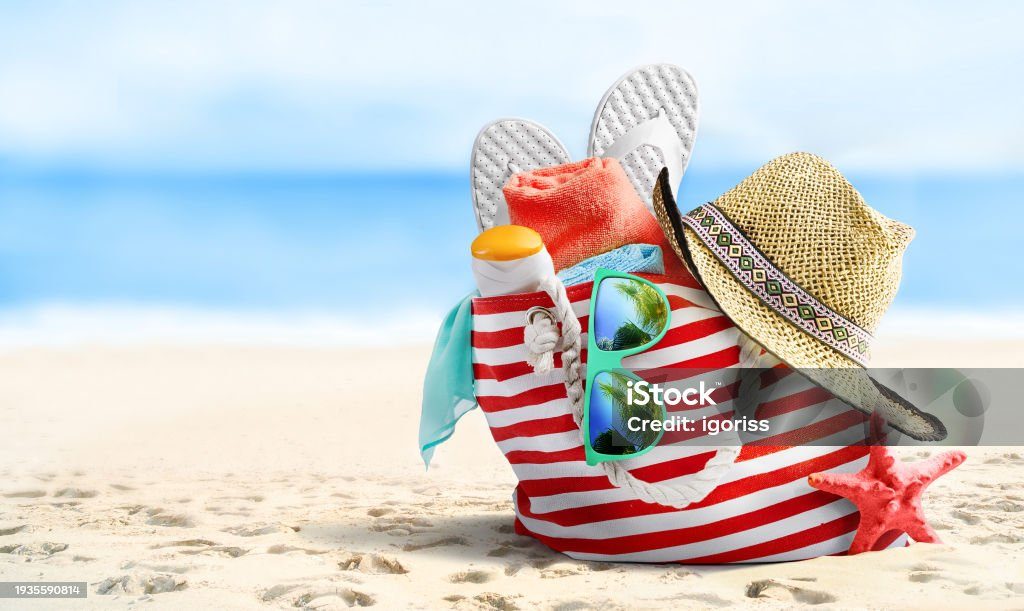 Striped beach bag with hat and flip-flops on the sand